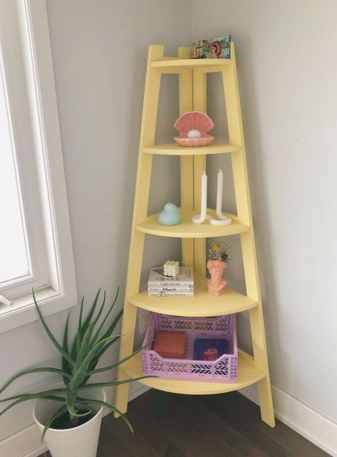 a yellow shelf next to a potted plant in a room with white walls and wooden floors