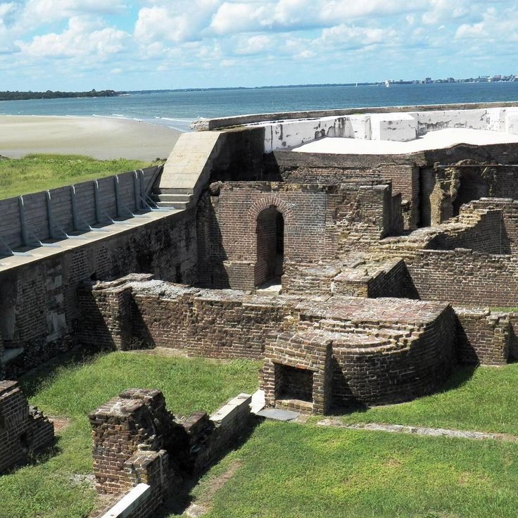 an old brick building sitting on top of a lush green field next to the ocean