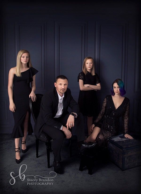 a group of people posing for a photo in black outfits and one woman is sitting on a chair