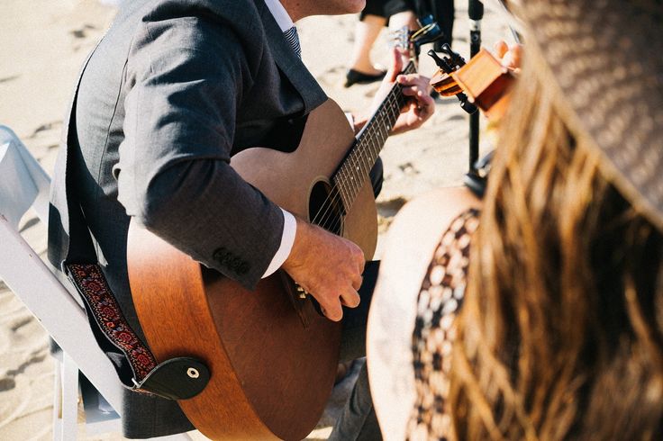 a man sitting on top of a chair holding a guitar next to a woman wearing a hat