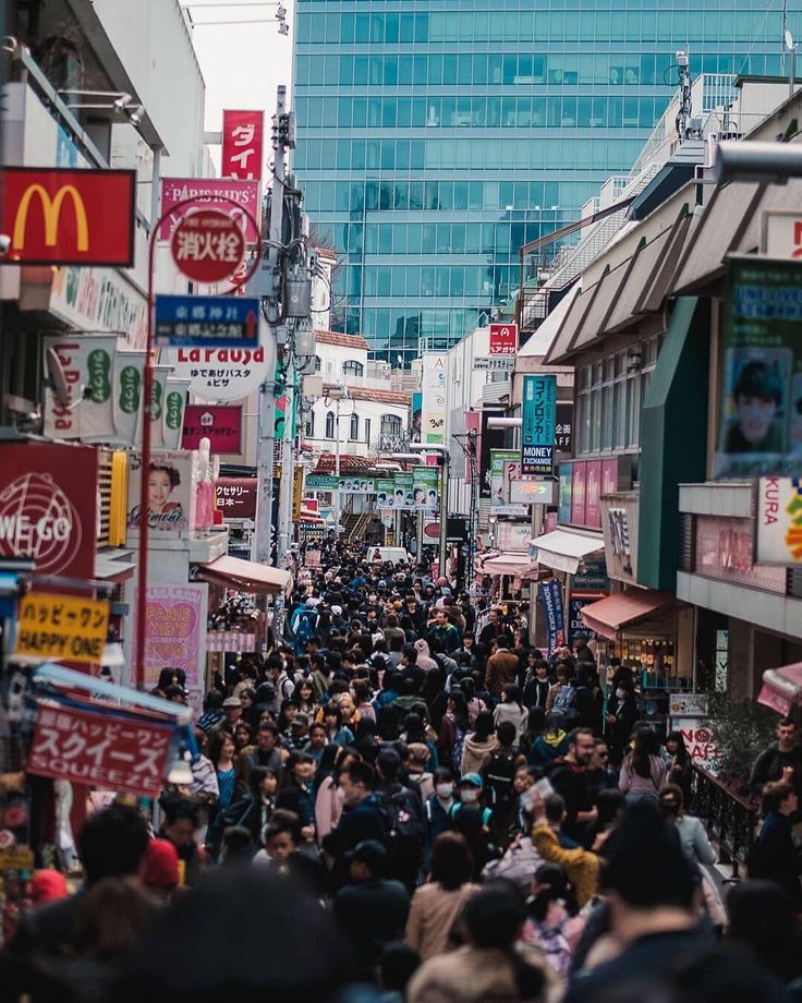 a crowded city street filled with lots of people walking down one side of the road