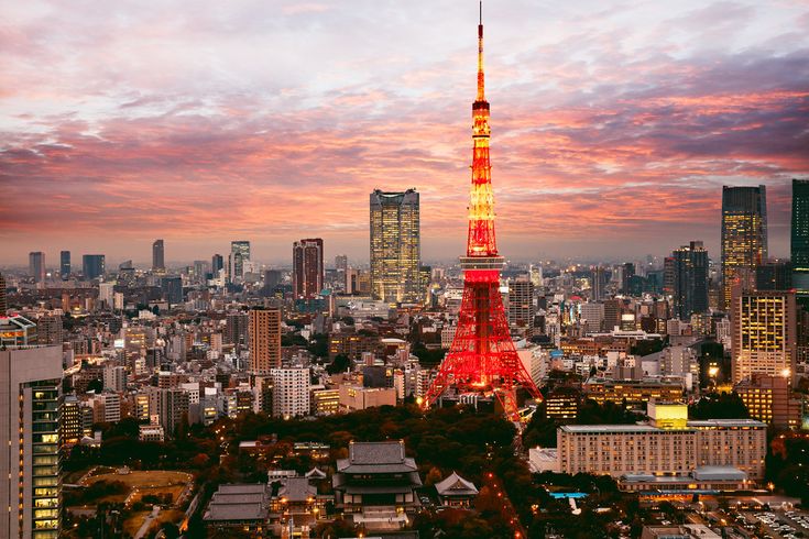 the eiffel tower is lit up in red and yellow at night, with other tall buildings behind it