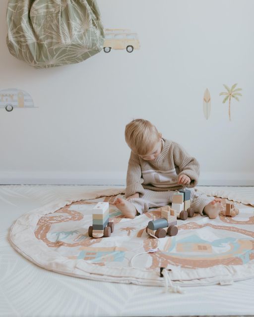 a toddler playing with wooden blocks on the floor in front of a white wall