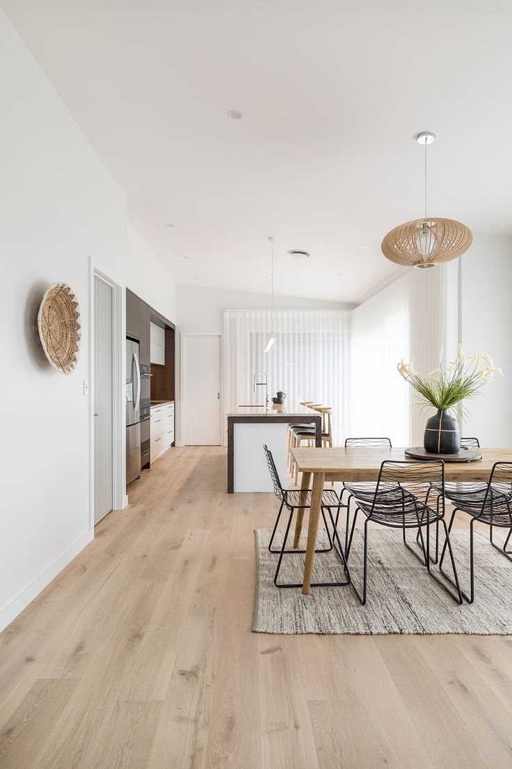 a dining room table and chairs in front of an open kitchen area with white walls