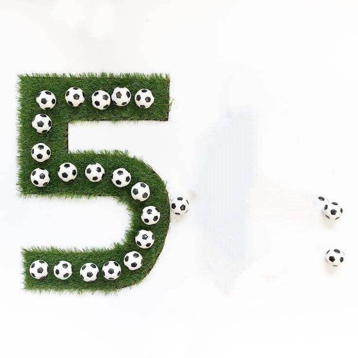 the number five is made out of grass with soccer balls on it and surrounded by smaller ones