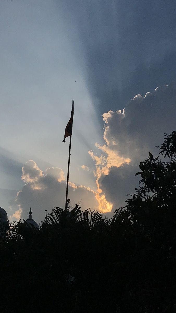 the sun shines through clouds behind a flag pole in front of some bushes and trees