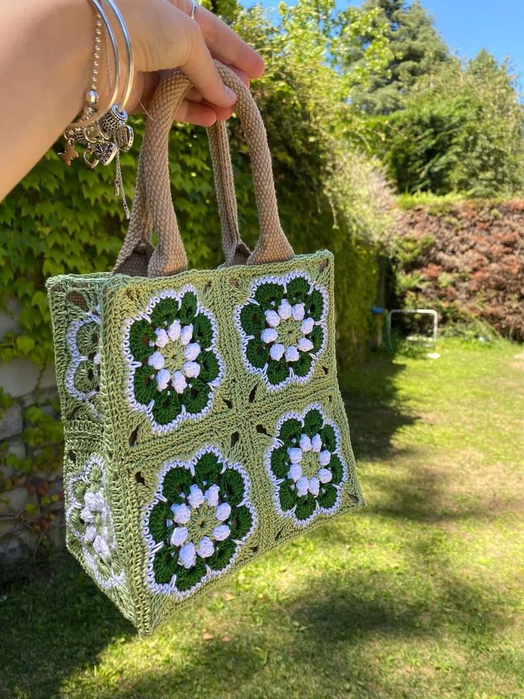 a hand holding a green crocheted bag with flowers on the front and sides