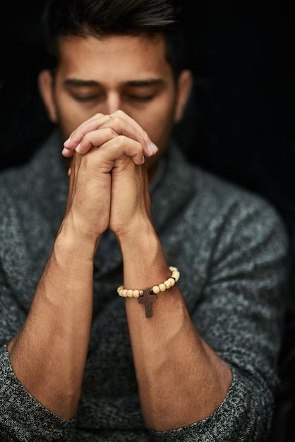 a man with his hands folded in prayer, looking down at the ground while wearing a bracelet