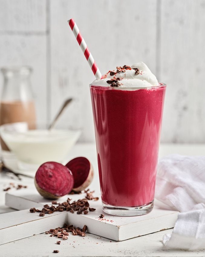 a red drink with whipped cream and chocolate sprinkles on the table next to it