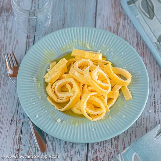 a blue plate topped with pasta on top of a wooden table next to silverware