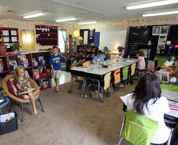 children are sitting in chairs and reading books at the library with adults standing around them