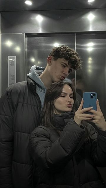 a man and woman standing in front of a mirror looking at their cell phones together