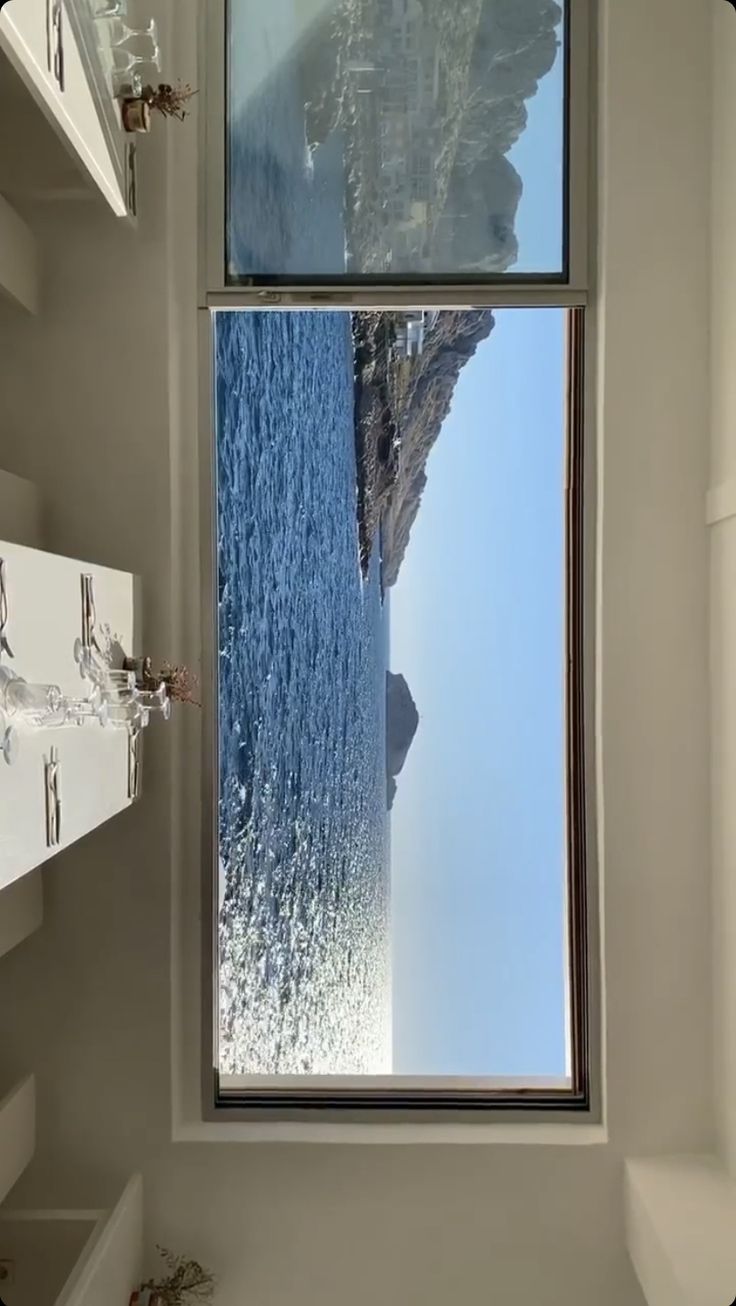 a bathroom with a large window that looks out to the ocean and mountains in the distance