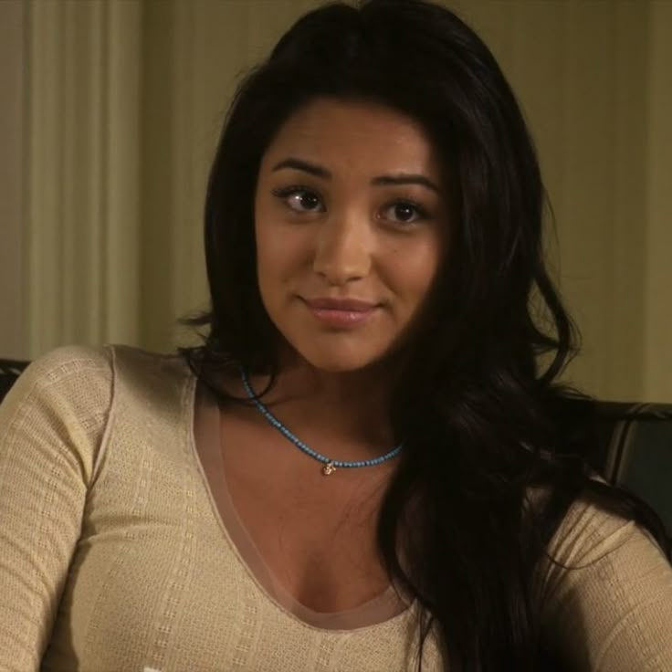 a woman with long dark hair wearing a blue beaded necklace sitting in a chair