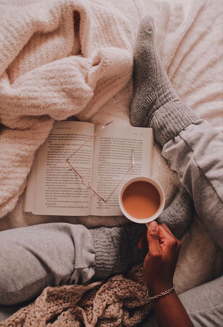 a person laying in bed holding a cup of coffee and an open book with their hands