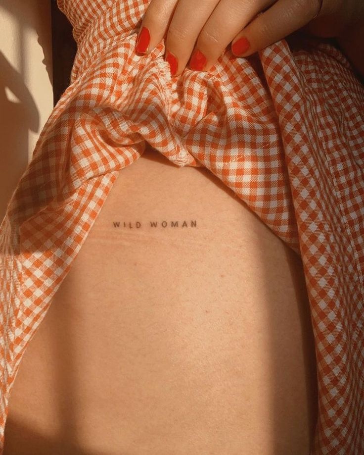 a woman's back with the words wild woman tattooed on her lower back and an orange gingham dress