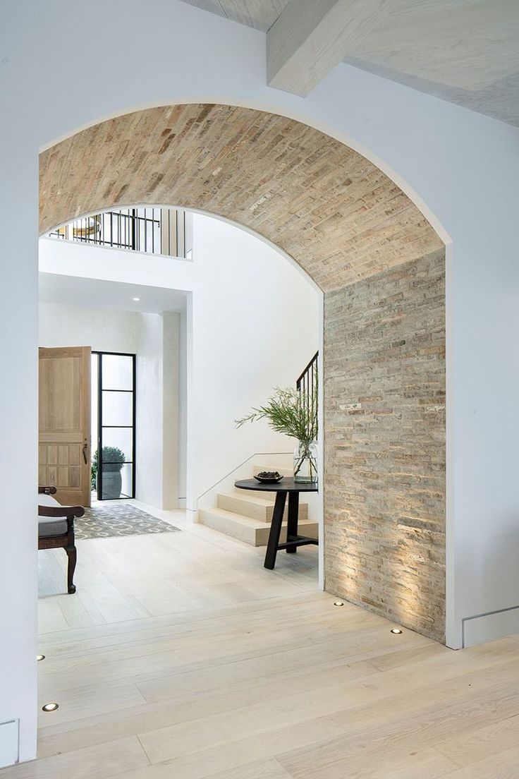 an arched doorway leads to a living room with white walls and hardwood floors, along with a table that has a plant on it