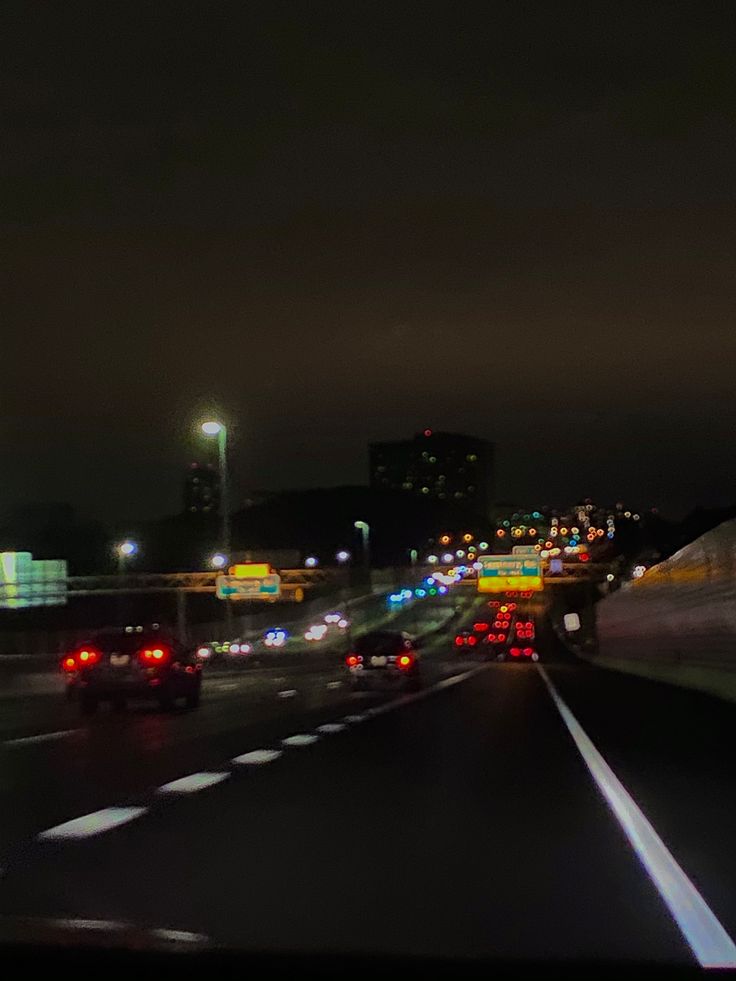 cars are driving down the highway at night with city lights in the backgroud