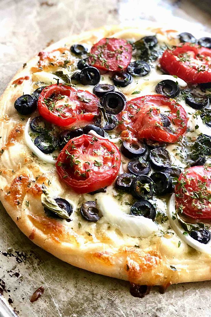 a pizza with tomatoes, olives and mozzarella on it sitting on a baking sheet