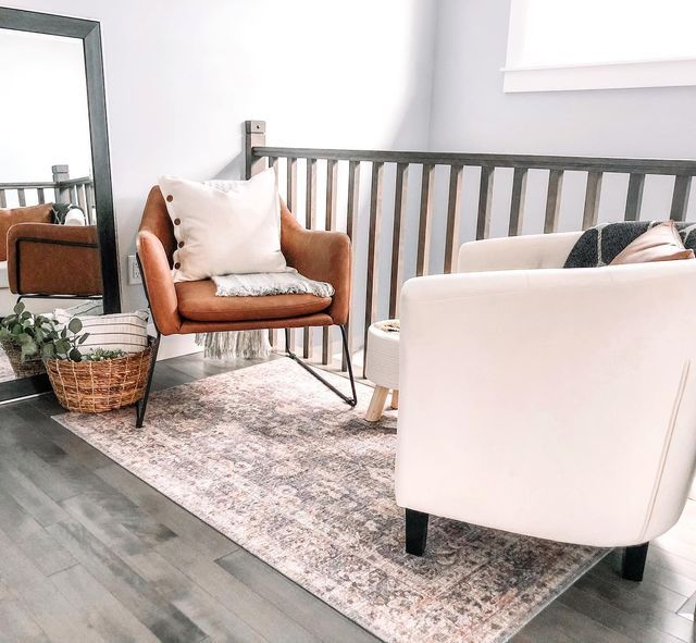 a living room with two chairs and a rug in front of a large mirror on the wall