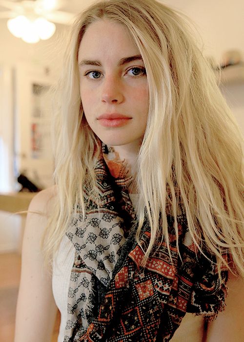 a woman with long blonde hair is posing for the camera, wearing a scarf around her neck