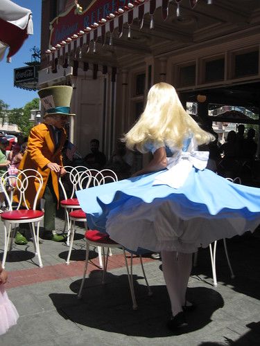 a woman dressed as a doll sitting at a table with an umbrella over her head