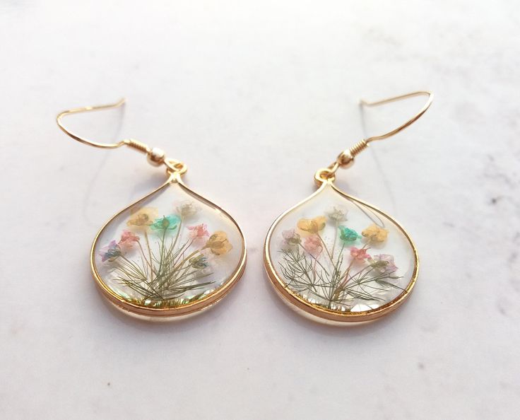 a pair of earrings with flowers in them on a marble surface, hanging from gold earwires