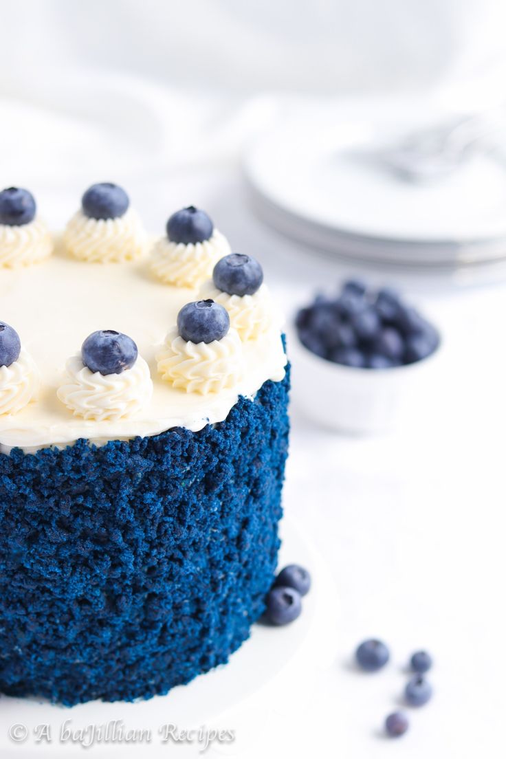 a blue velvet cake with white frosting and blueberries on top, sitting on a plate