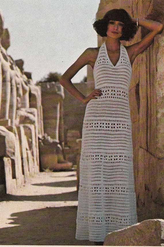 a woman in a white crocheted dress standing next to an ancient building