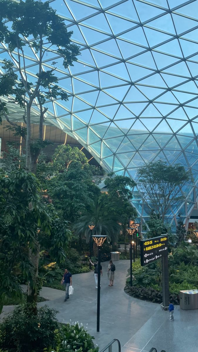 the inside of a building with lots of plants and people walking around in front of it