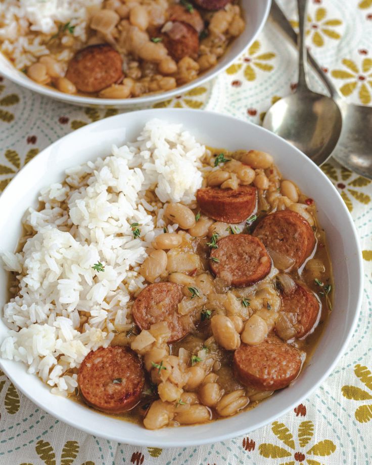 two bowls filled with beans and sausage next to white rice on a tablecloth covered table