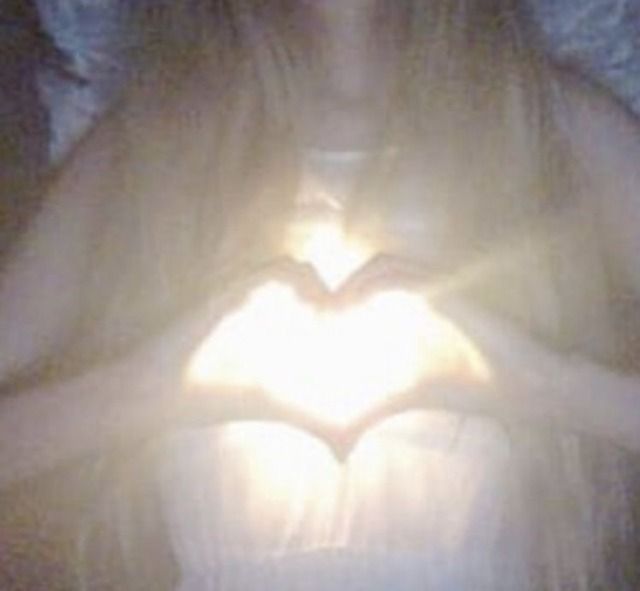 a woman holding her hands in the shape of a heart with light shining through it