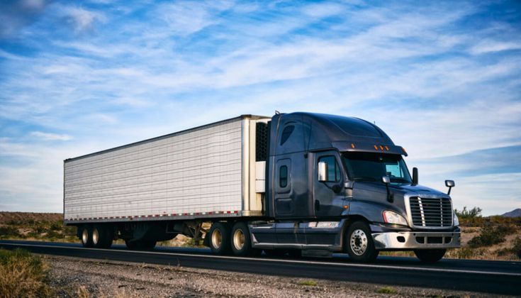 a semi truck driving down the road in the middle of the desert with blue sky and clouds