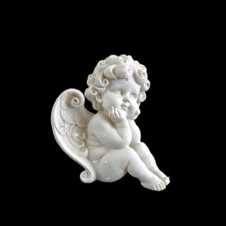 a small white angel statue sitting on top of a black surface with its hands to her face