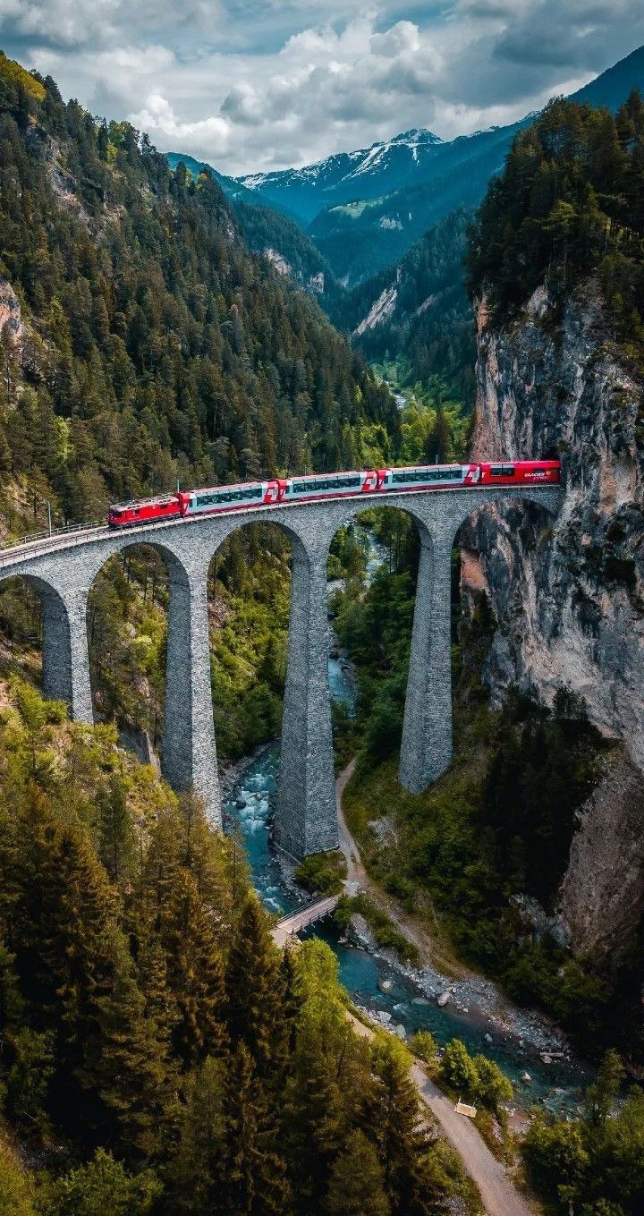 a train traveling over a bridge with mountains in the backgrouund and trees on both sides