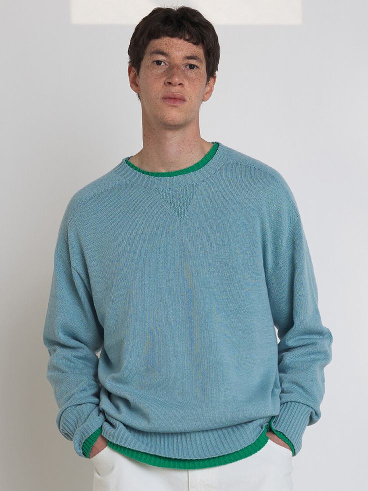 a man standing in front of a white wall wearing a blue sweater and white pants