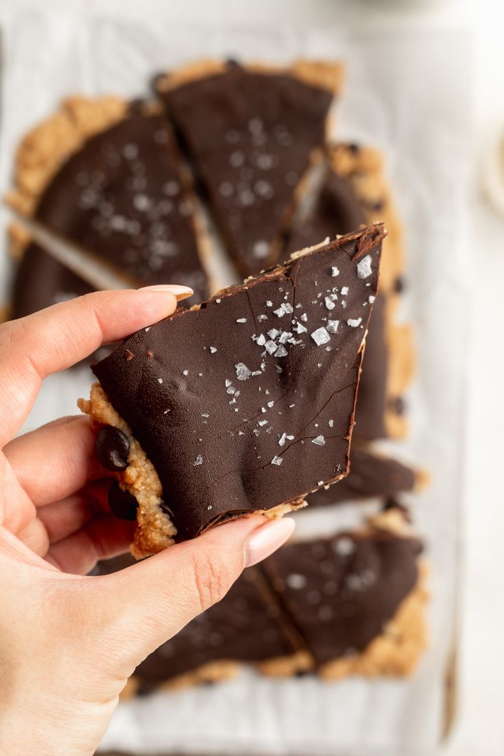 a person holding up a piece of chocolate tart on top of a white table