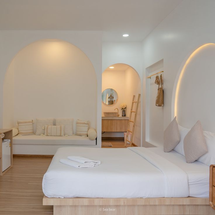 a bedroom with white walls and wood flooring has a bed in the middle, an arched doorway leading to another room