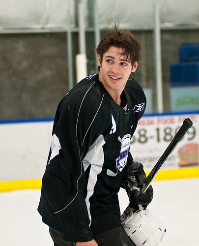 a young man in black and white jersey holding a hockey stick on an ice rink