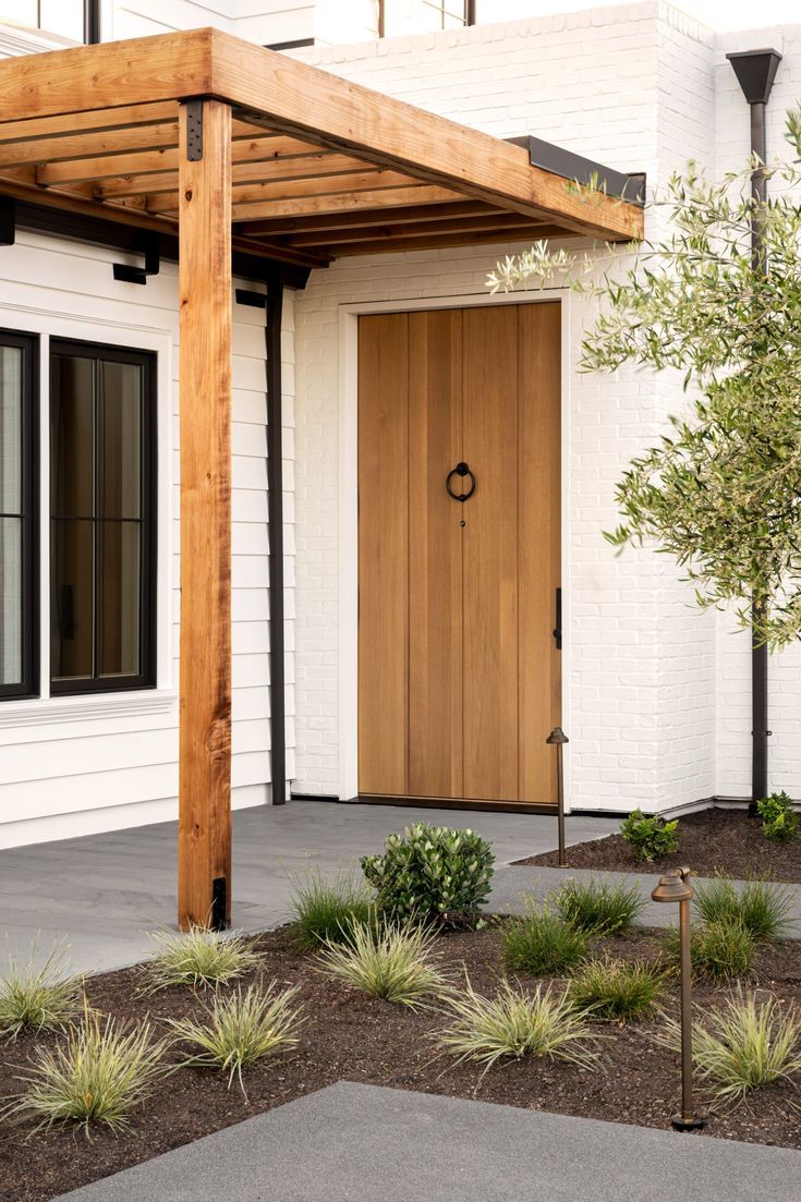 a white house with a wooden front door and pergolated planters in the foreground