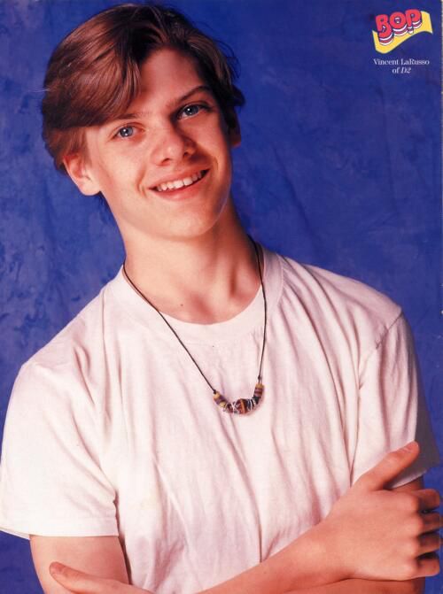 a young man wearing a white shirt and necklace