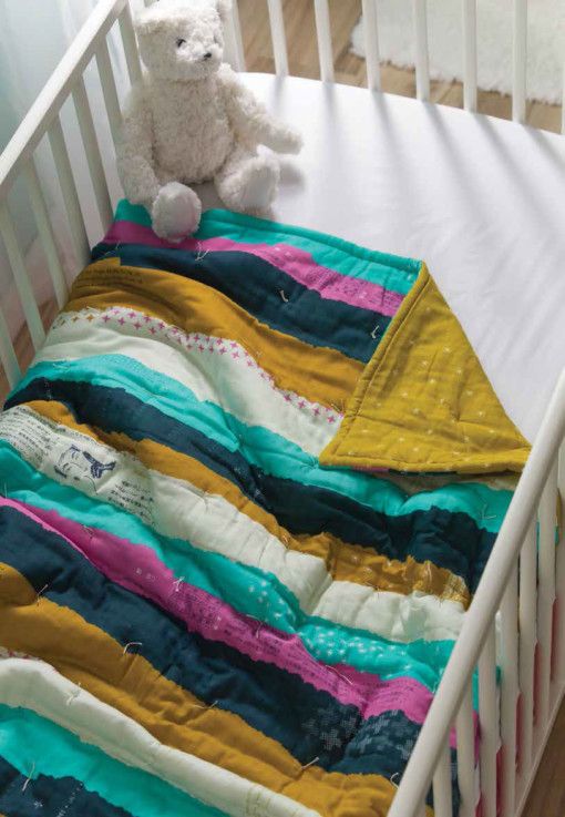 a baby crib with a teddy bear sitting on top of it and a blanket draped over the crib