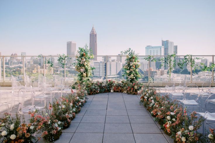 an outdoor ceremony setup with white chairs and floral arrangements on the top of a roof