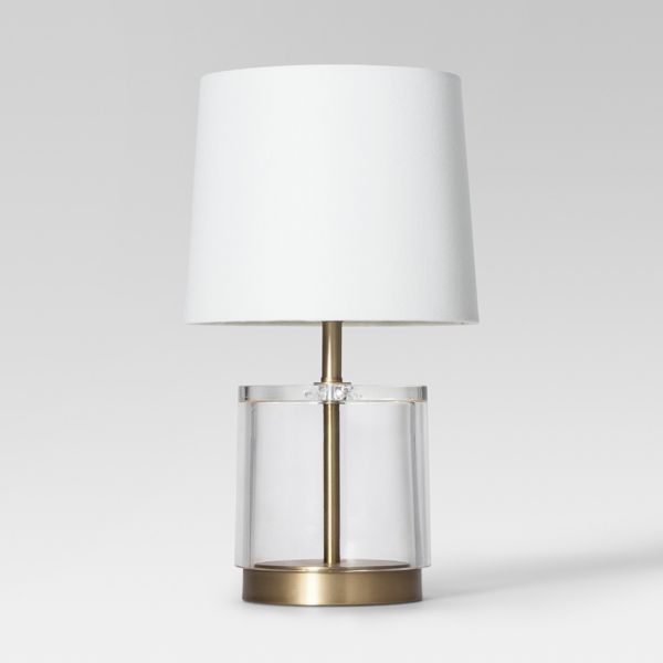 a table lamp with a white shade on the base and a gold metal frame around it