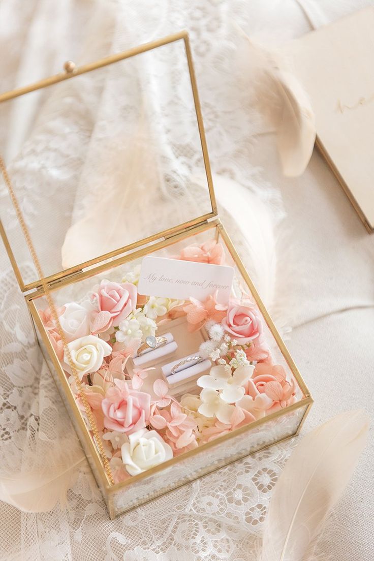 an open box with flowers and feathers on a lace tablecloth next to a feather quill