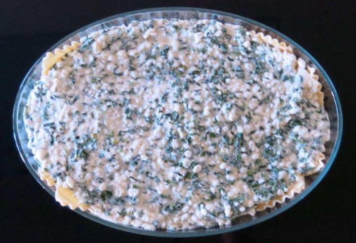 a pie with spinach and cheese on top in a glass dish sitting on a black surface