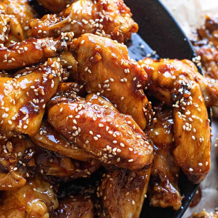 chicken wings covered in sesame seeds and sesame seeds on top of a black plate with sauce