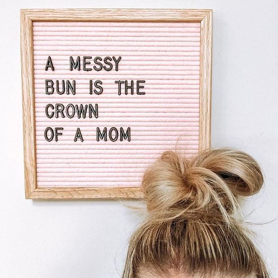 a woman with her hair in a messy bun is next to a framed sign that says, a messy bun is the crown of a mom