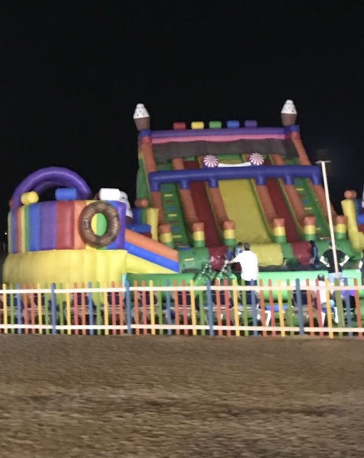 a large inflatable bounce house with people standing around it at night, near a fence