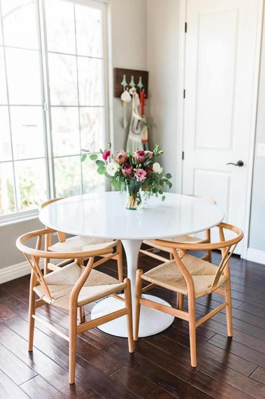 a white table and chairs in a room with wooden floors, windows, and artwork on the wall